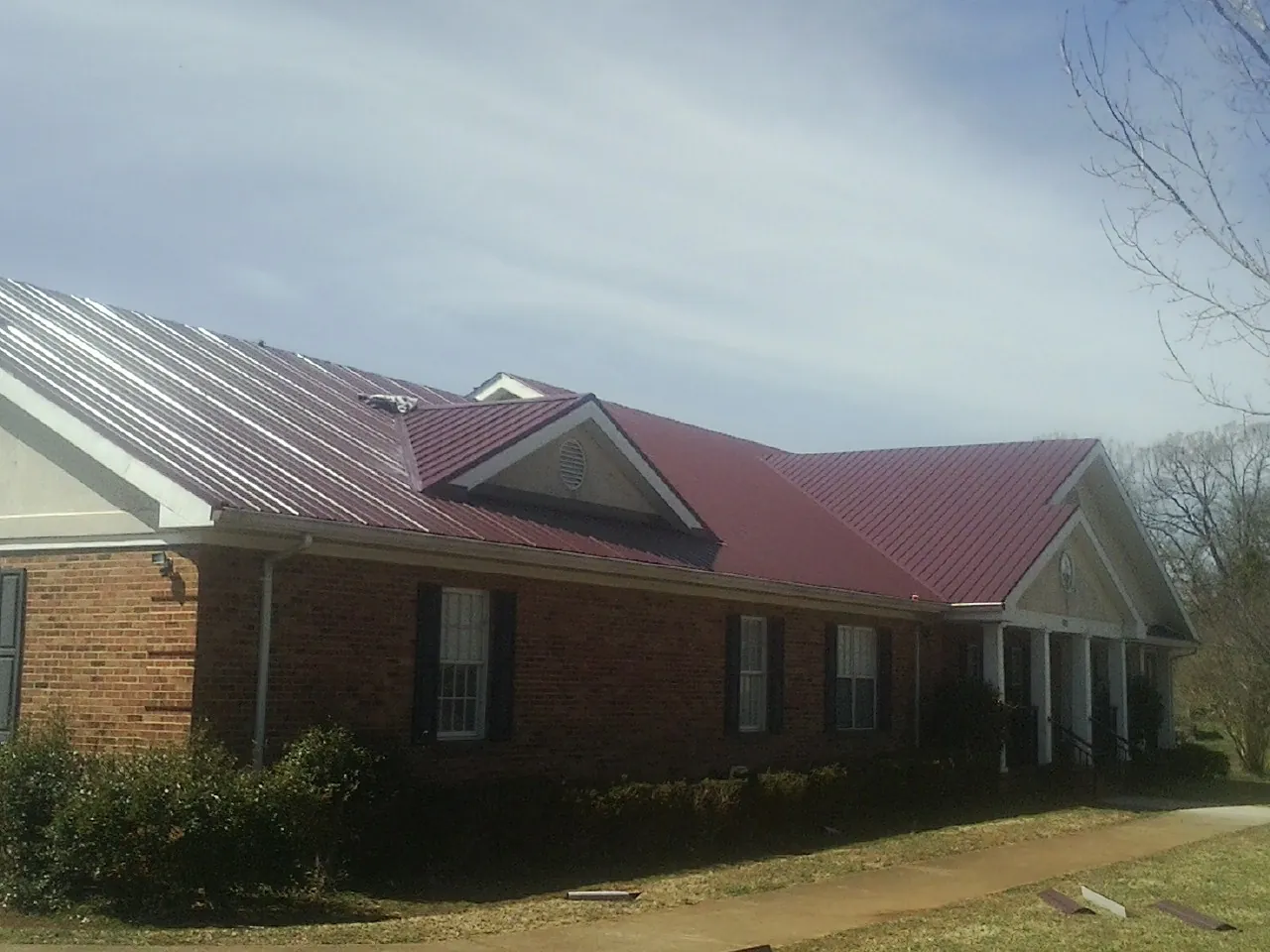 Red metal roof with gabled entries on a long brick building, from a Hail Damage Roof Repair job in Camp Hill