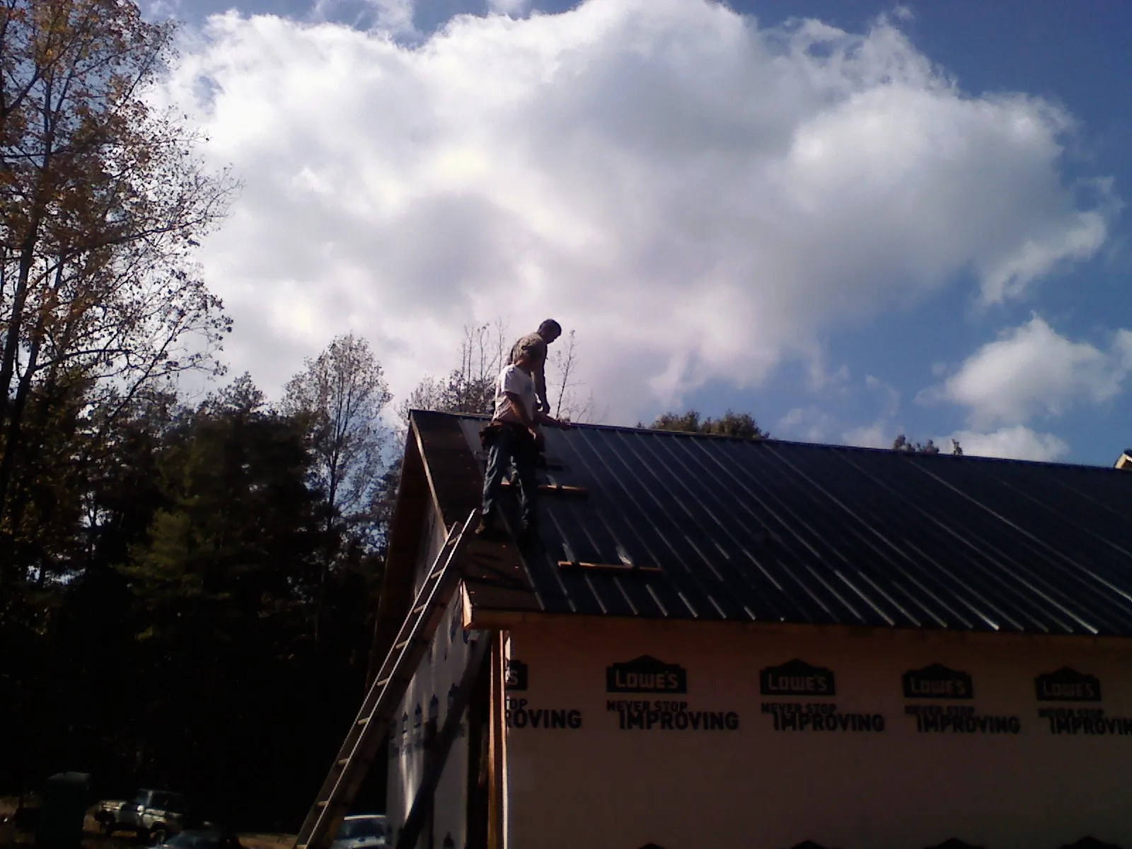 Roofer fastening dark metal panels high against a cloudy sky, from a Roof Inspection job in Camp Hill
