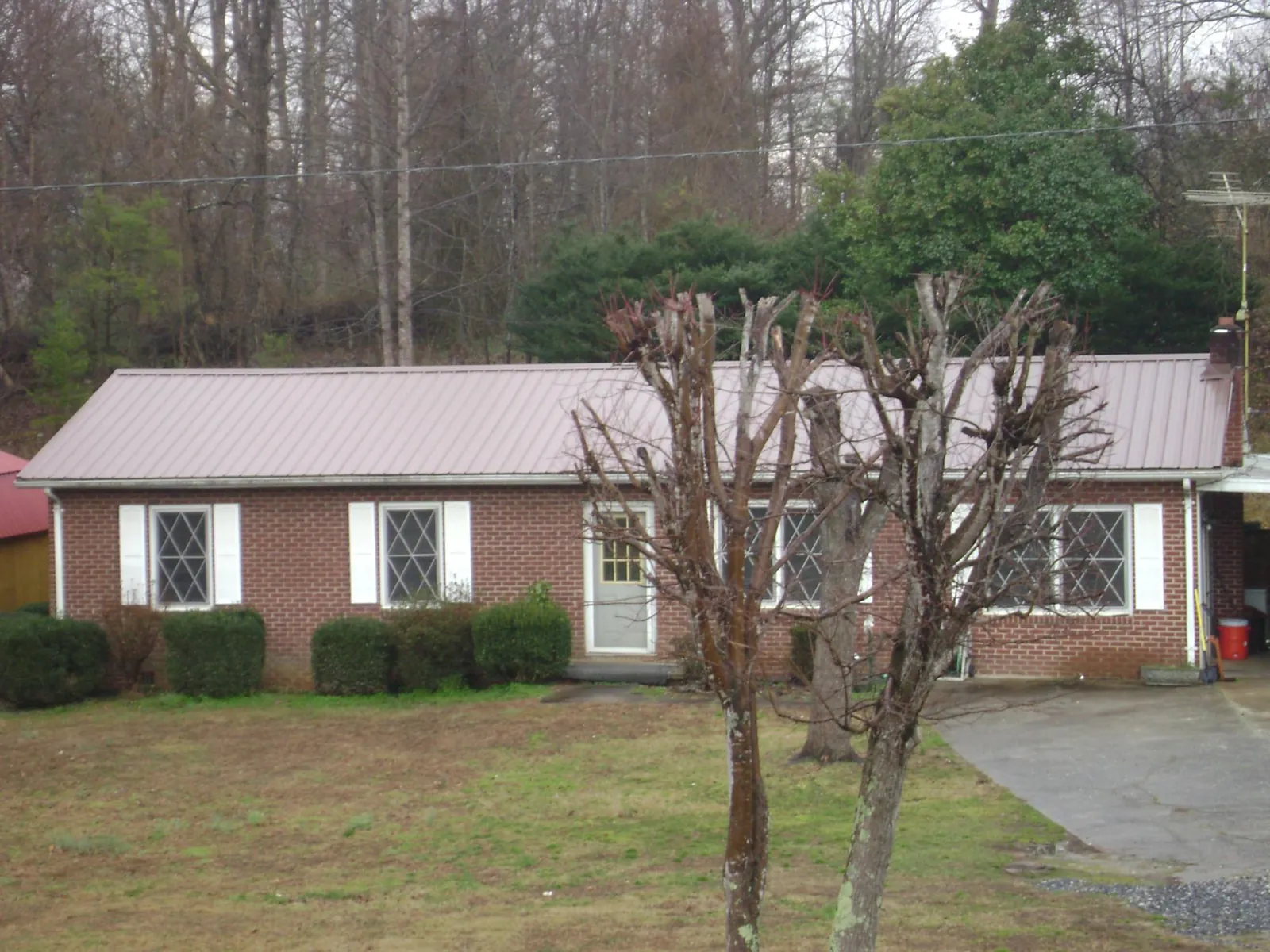 Mauve metal roof on a brick ranch home behind bare trees in Camp Hill