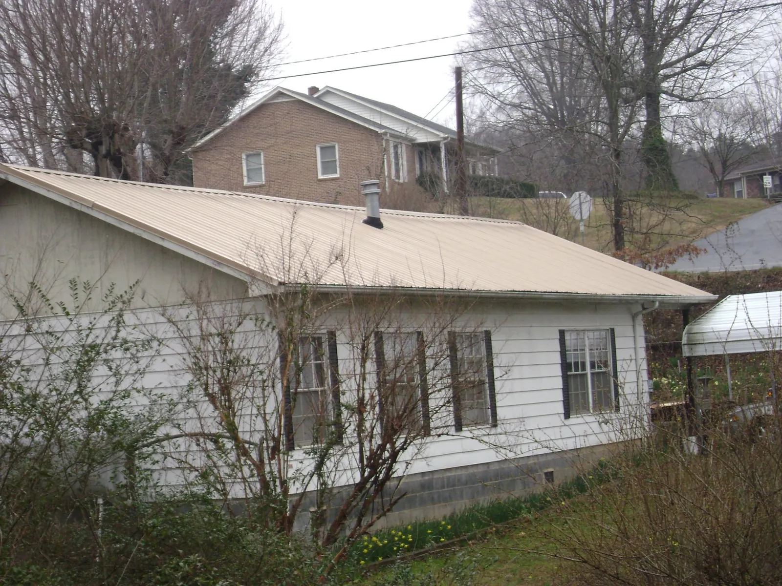 Tan metal roof on a white sided house set into a hillside — Commercial Roofing by Roofing Brothers in Camp Hill