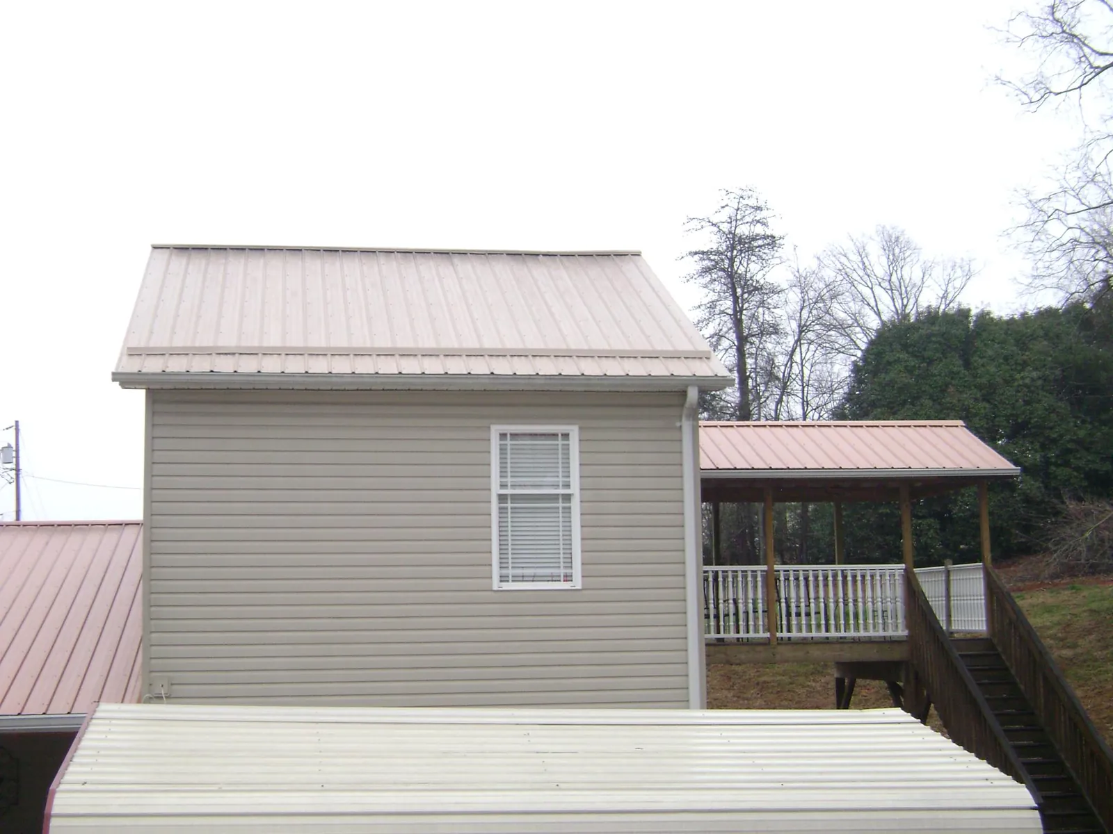 Tan metal roofs on a two story addition and attached porch, from a Roof Replacement job in Camp Hill